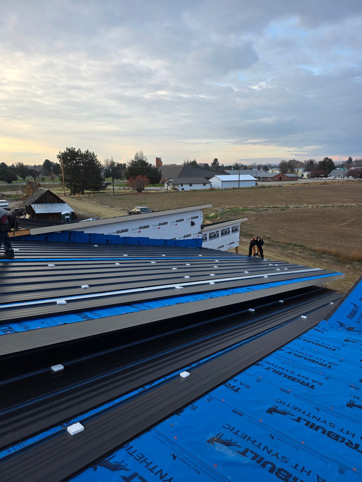 Standing seam metal roof install in progress over synthetic underlayment