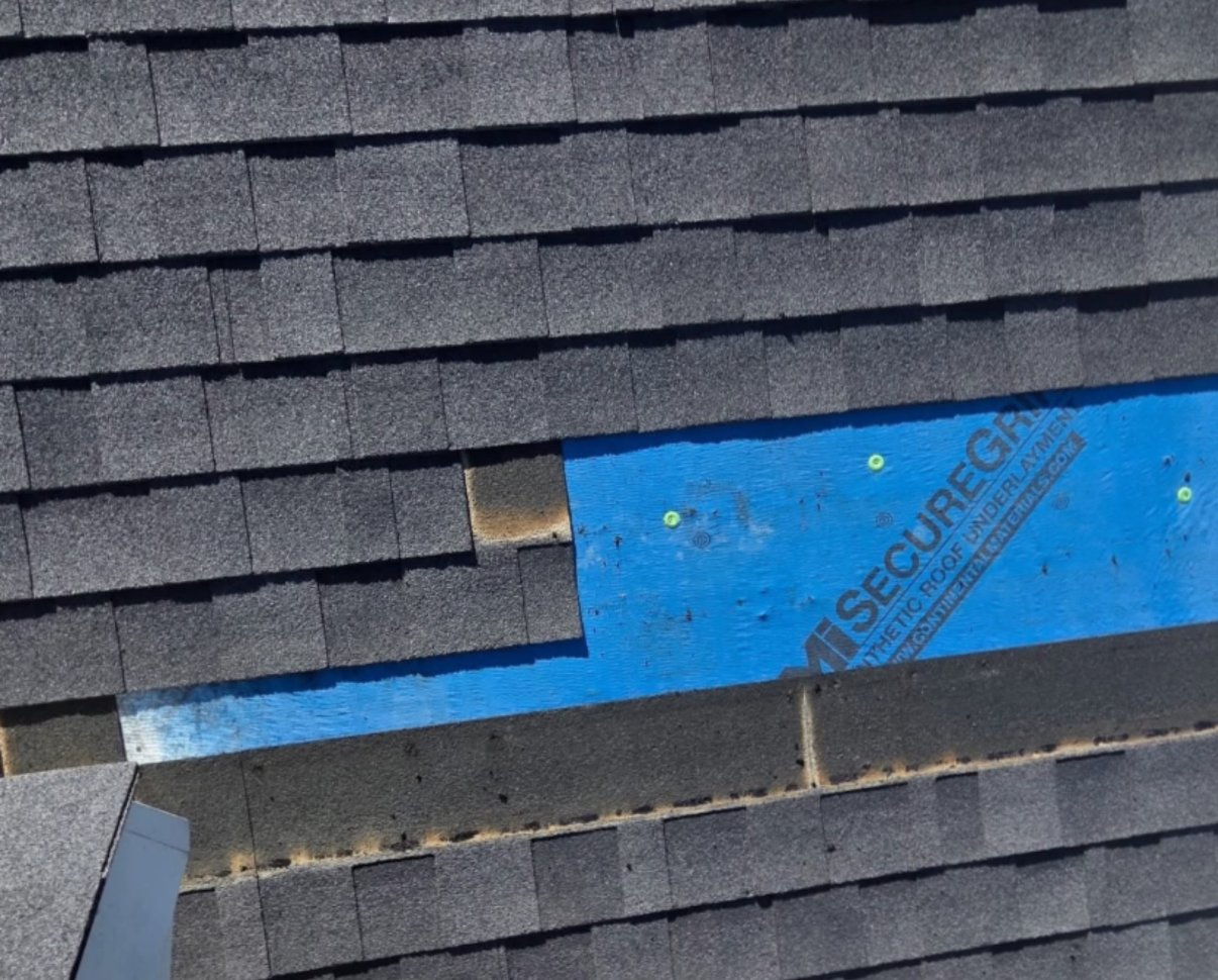 Asphalt shingle roof repair in progress with synthetic underlayment exposed